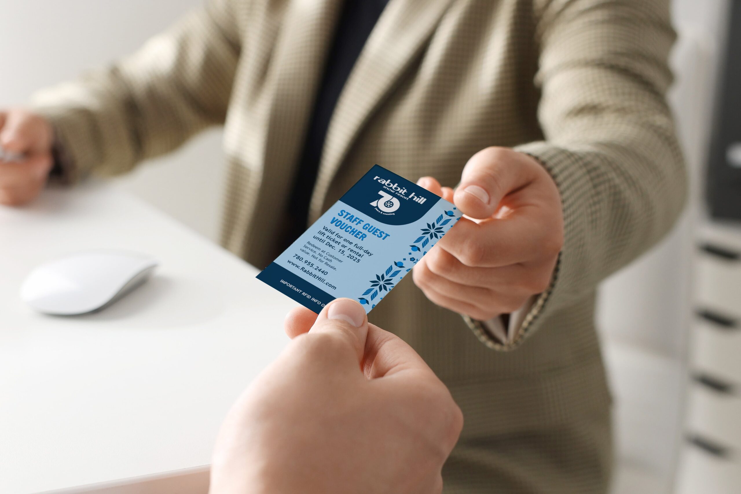 Person handing a 70th anniversary branded staff guest voucher to another person